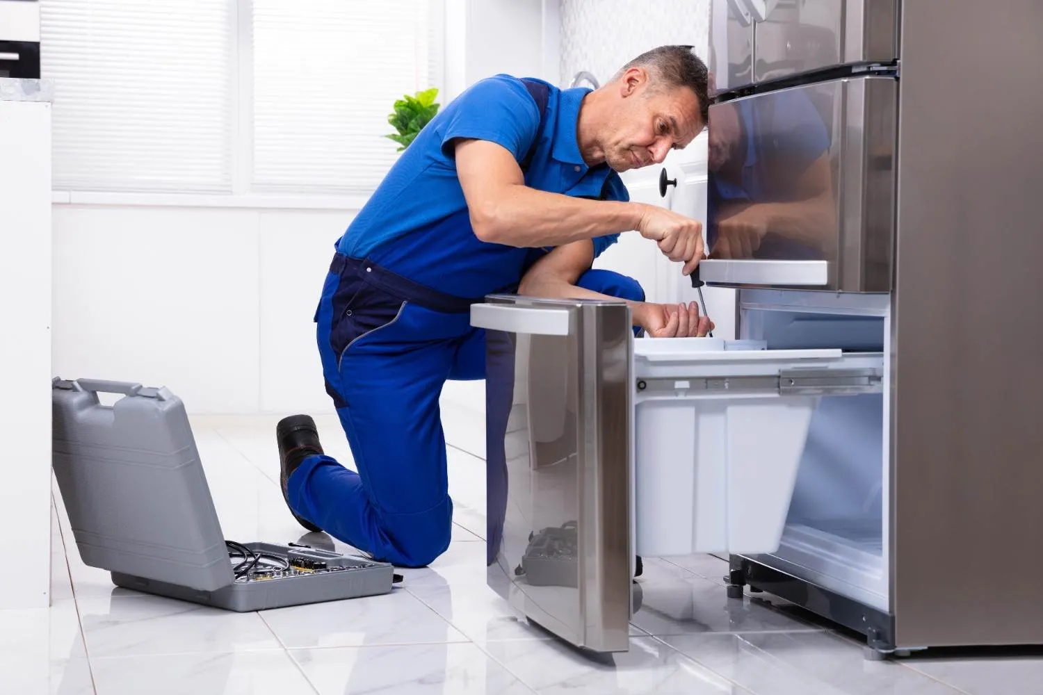 Technician kneeling to repair the drawer of a stainless steel refrigerator